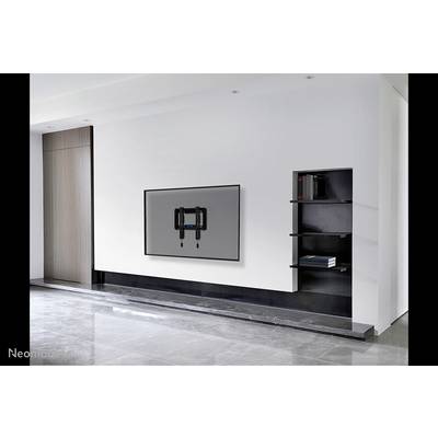 Flachbildfernseher an einer modernen weißen Wand montiert, linke Seite mit Holzpaneel, rechter eingebauter Regalbereich mit Büchern.