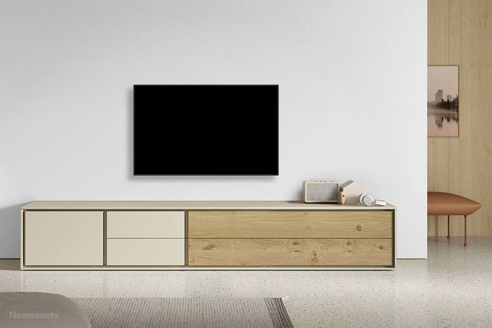 Ein minimalistisches Wohnzimmer mit einem Wandfernseher über einem modernen Holzschrank. Ein Lautsprecher und ein gerahmtes Bild sind darauf platziert.