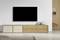 Ein flacher Fernseher an einer weißen Wand, darunter ein minimalistisches Holz- und Hellbeige-Sideboard mit drei Schubladen und zwei Türen.