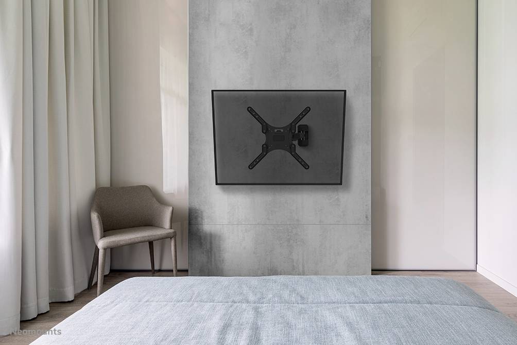 Ein modernes Schlafzimmer mit einem Fernseher an der Wand, einem Sessel in der Ecke und einem Bett im Vordergrund.