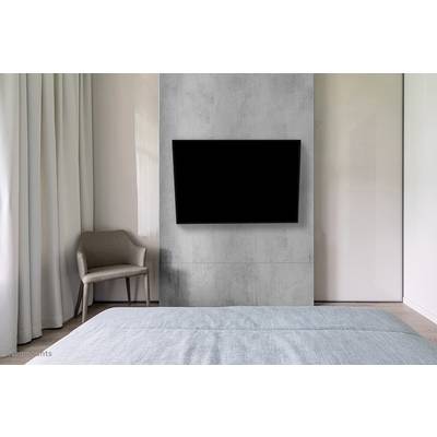 Ein modernes Schlafzimmer mit einem Fernseher an der Wand, einem Stuhl und einem Bett im Vordergrund. Neutrale Farben dominieren den Raum.