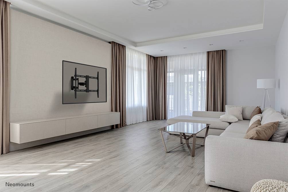 Ein modernes Wohnzimmer mit hellgrauem Sofa und Glastisch; an der Wand eine TV-Halterung ohne Fernseher, große Fenster mit Vorhängen.