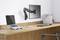 'Moderner Arbeitsplatz mit Laptop, Monitor an schwenkbarem Arm, Tastatur und Maus auf einem Holztisch. Aktenordner im Hintergrund.'