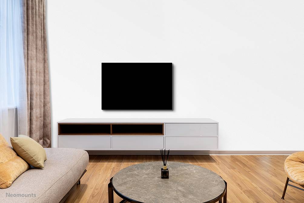 Wohnzimmer mit hellem Holzboden, grauem Sofa, runden Tisch, weißem TV-Möbel und schwarzem Flachbildfernseher an der Wand.