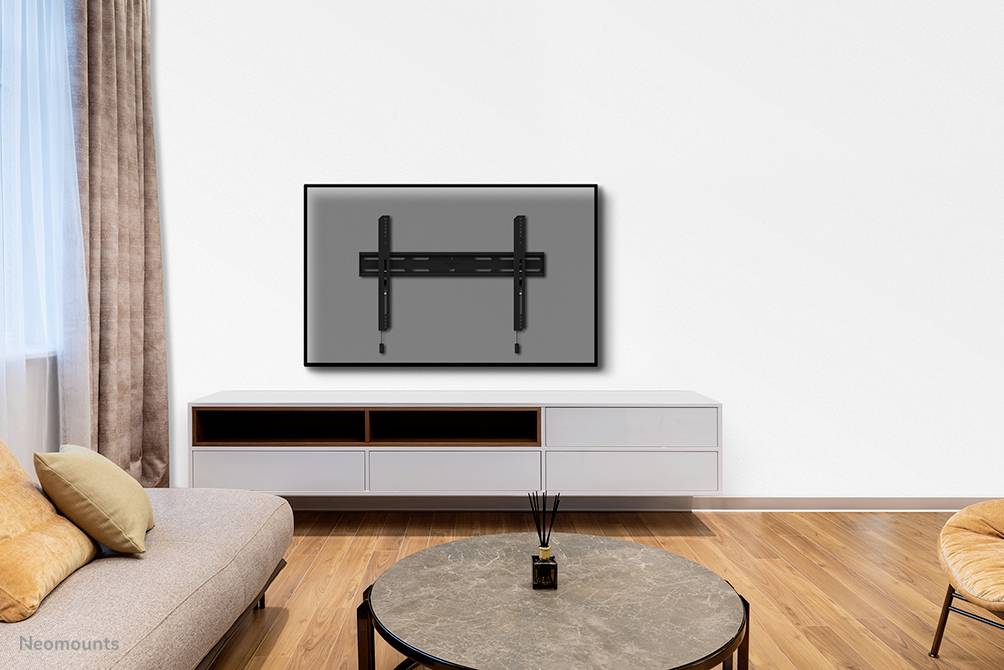 Ein Wohnzimmer mit Sofa, Couchtisch und einem großen TV an der Wand. Helle Holzböden und ein Fenster mit braunem Vorhang links.