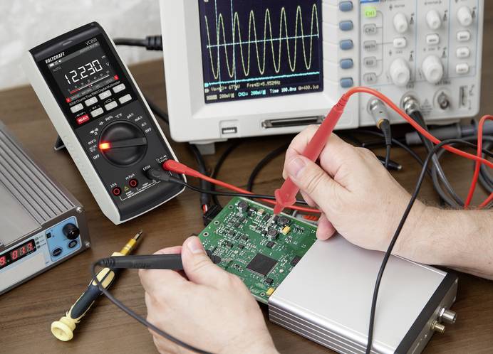 Labortisch mit Voltcraft Multimeter, Labornetzgerät, Oszilloskop und Prüfobjekt. Mit den beiden Messkontakten wird an einer Platine gmessen.
