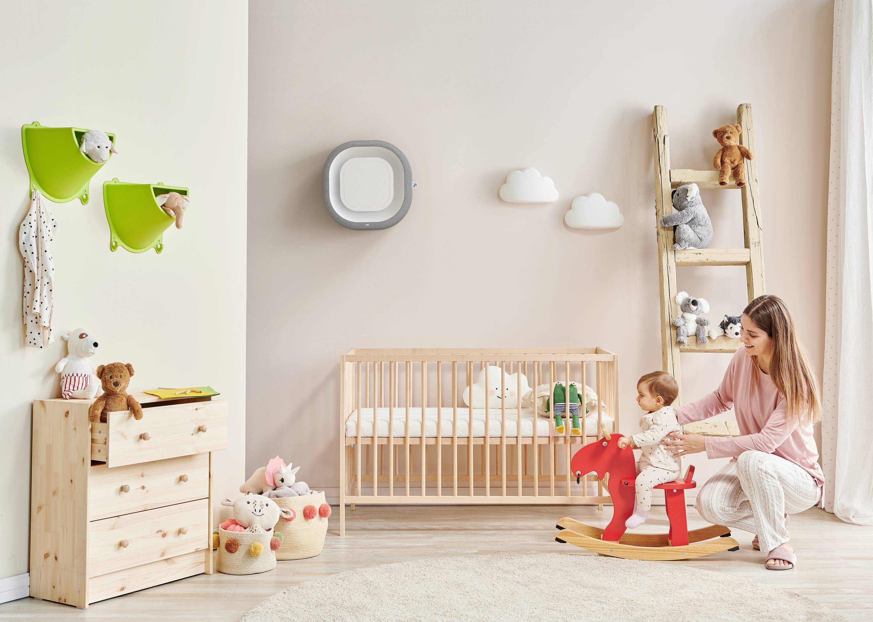 Eine Mutter spielt mit ihrem Kind, das auf einem roten Schaukelpferd sitzt. Im Hintergrund ein Kinderbett und Spielzeug.