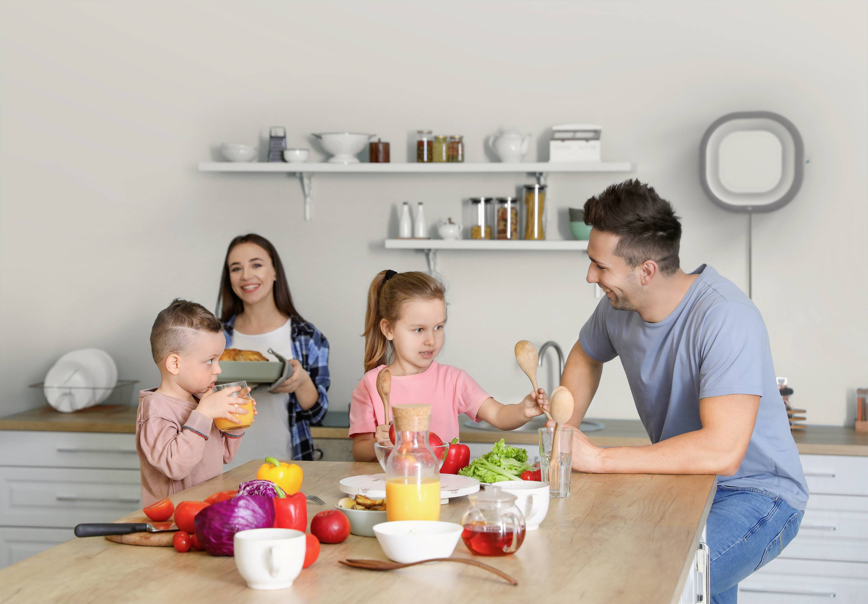 Familie in moderner Küche: Vater und Tochter kochen zusammen, Mutter und Sohn bringen Zutaten. Fröhliche Atmosphäre beim gemeinsamen Kochen.