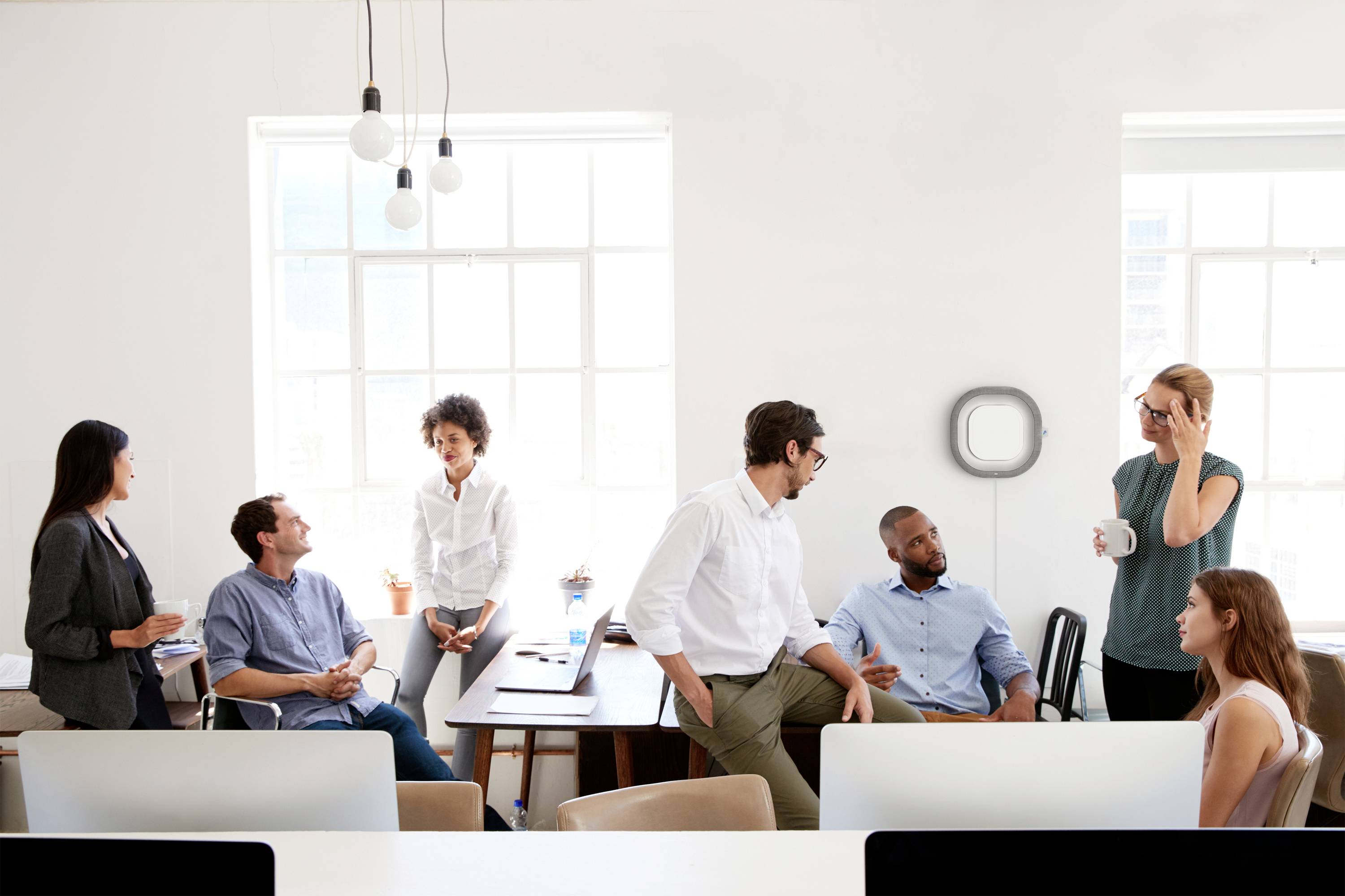 Eine Gruppe von acht Personen unterhält sich in einem modernen Büro mit großen Fenstern. Einige stehen, andere sitzen entspannt.