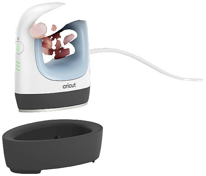 Eine Hand hält ein Cricut Mini-Bügeleisen über seine schwarze Basisstation. Das Gerät ist weiß und blau mit einem Netzkabel.