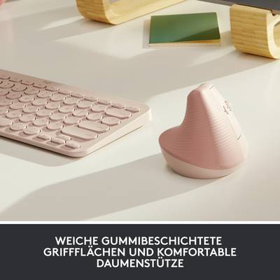 Vertikale rosa Computermaus und Tastatur auf einem Tisch. Der Text 'Weiche gummibeschichtete Griffflächen und komfortable Daumenstütze' betont komfortables Design.