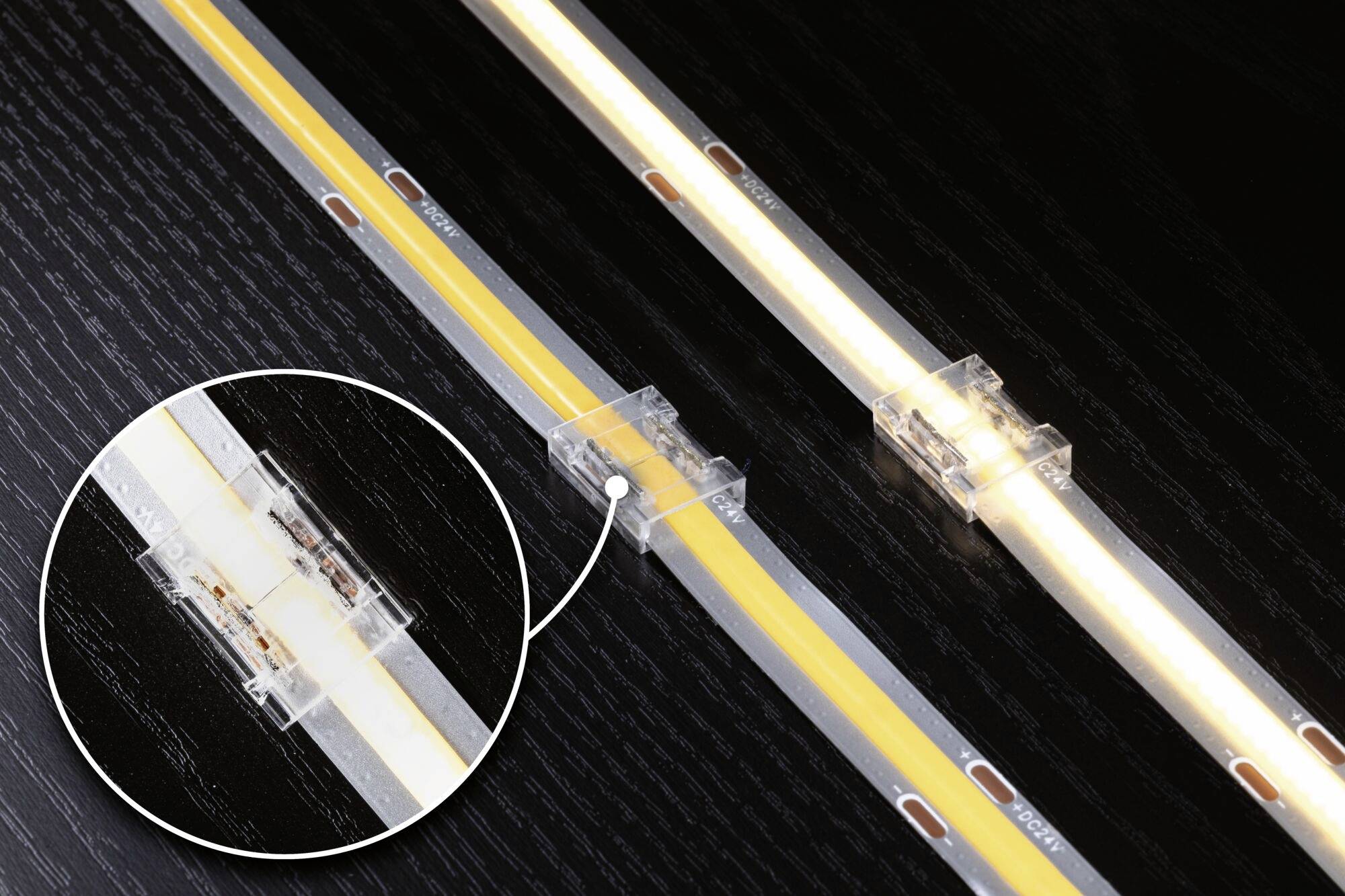 Zwei LED-Streifen auf schwarzem Hintergrund, verbunden durch transparente Clips, Detailansicht des Verbinders.