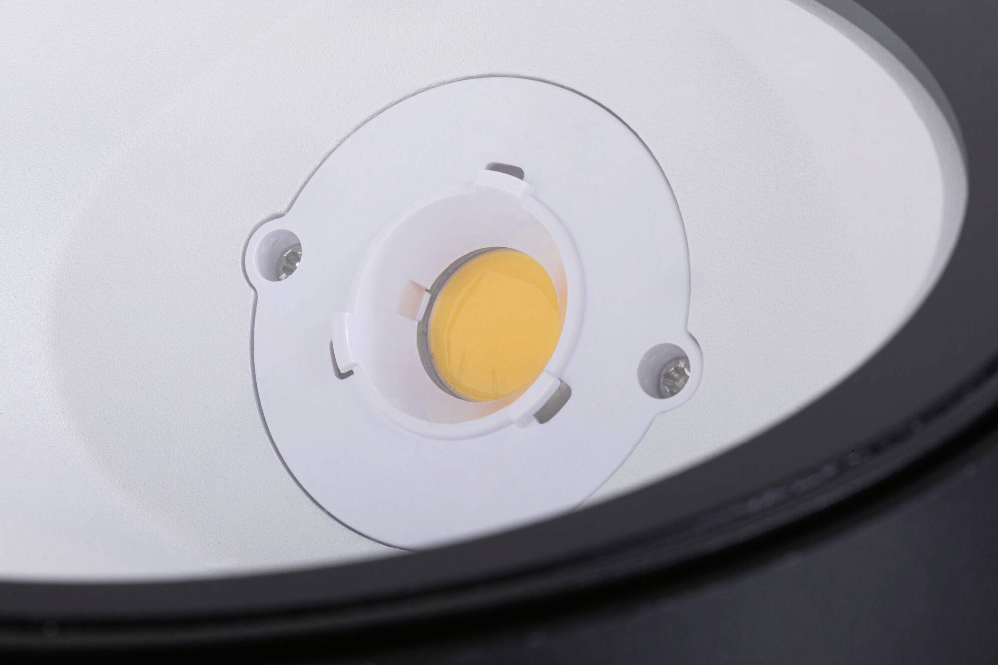 Nahaufnahme einer modernen LED-Leuchte mit kreisförmigem Design und zentralem gelbem LED-Chip, montiert in weißem Rahmen.