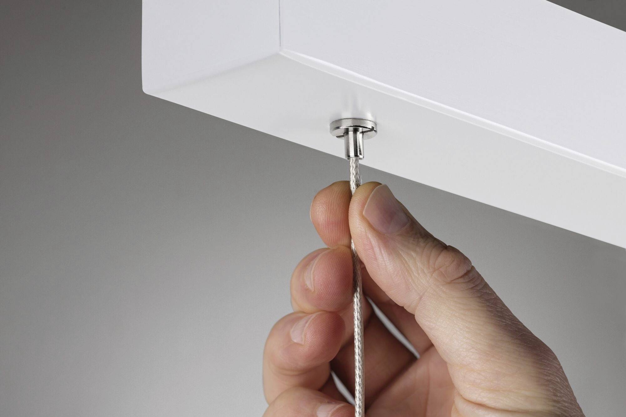 Hand zieht an Kabel aus rechteckiger Halterung an der Decke.
