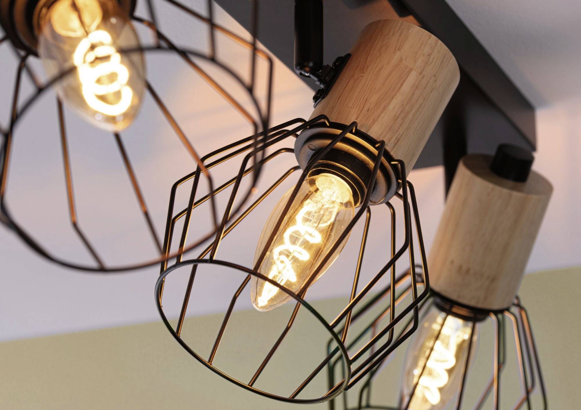 Nahaufnahme von drei dekorativen Glühbirnen in einem modernen Drahtkäfig-Design an einer Deckenleuchte, die warmes Licht ausstrahlen.