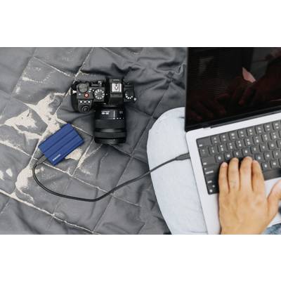 Eine Person arbeitet an einem Laptop, der an eine externe Festplatte angeschlossen ist. Daneben liegt eine Kamera auf einem grauen Tuch.