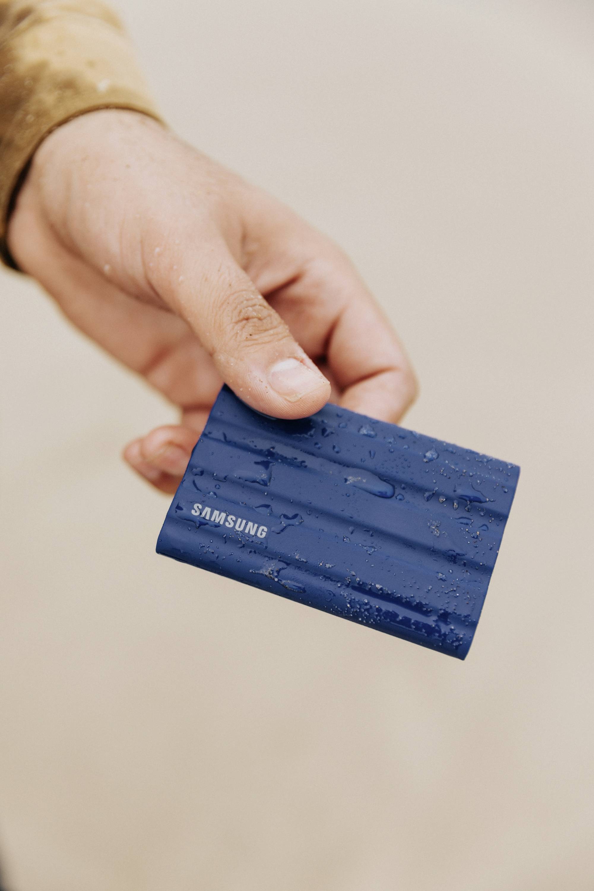 Eine Hand hält eine blaue, wasserfeste Samsung-Festplatte.