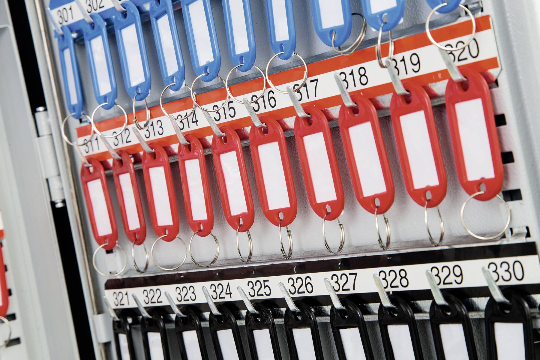 Ein Schlüsselkasten mit mehreren Reihen von farbigen Schlüsselanhängern: oben blau, in der Mitte rot und unten schwarz, nummeriert von 311 bis 330.