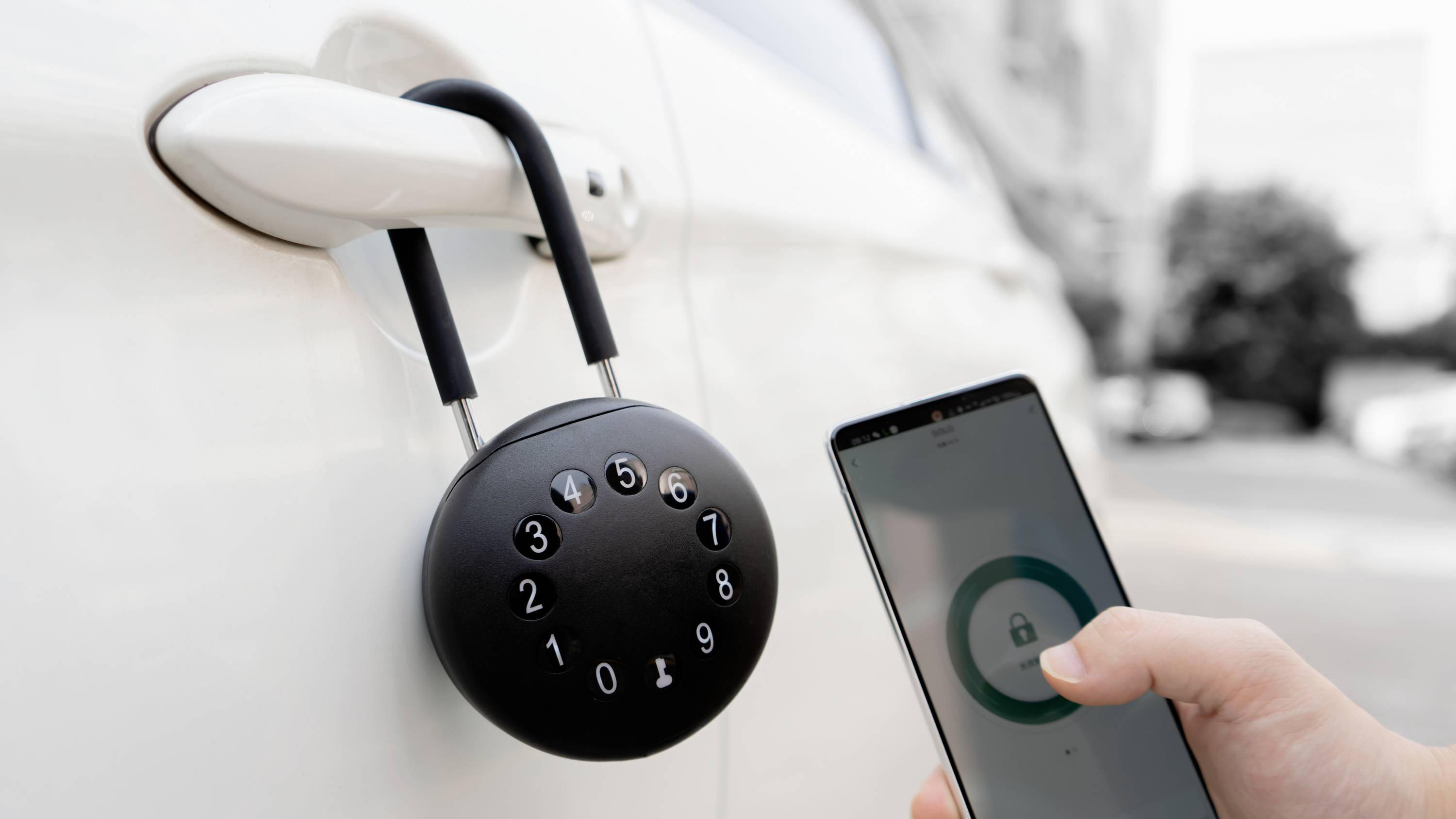 Eine Hand hält ein Smartphone, das eine offene Vorhängeschloss-Grafik zeigt. Ein Rundschloss mit Zahlen hängt an einer Autotür.