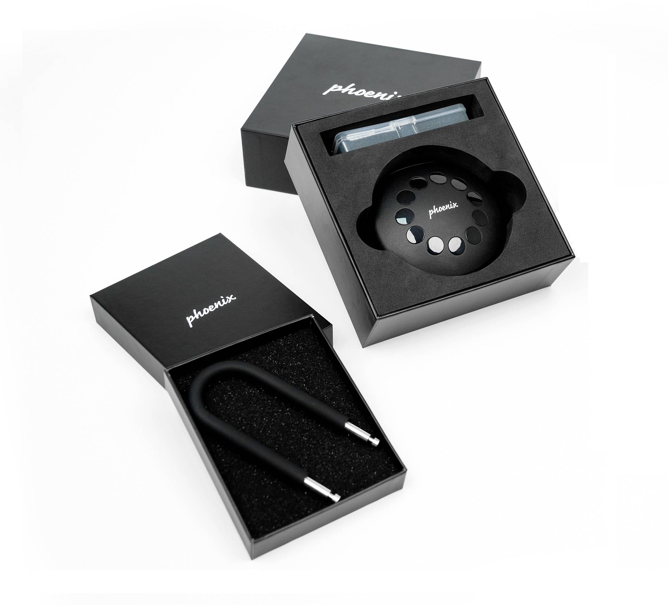 Zwei schwarze Produktverpackungen. Eine enthält ein Kabelschloss, die andere ein rundes Fahrradschloss mit Markenschriftzug 'phoeni.'.