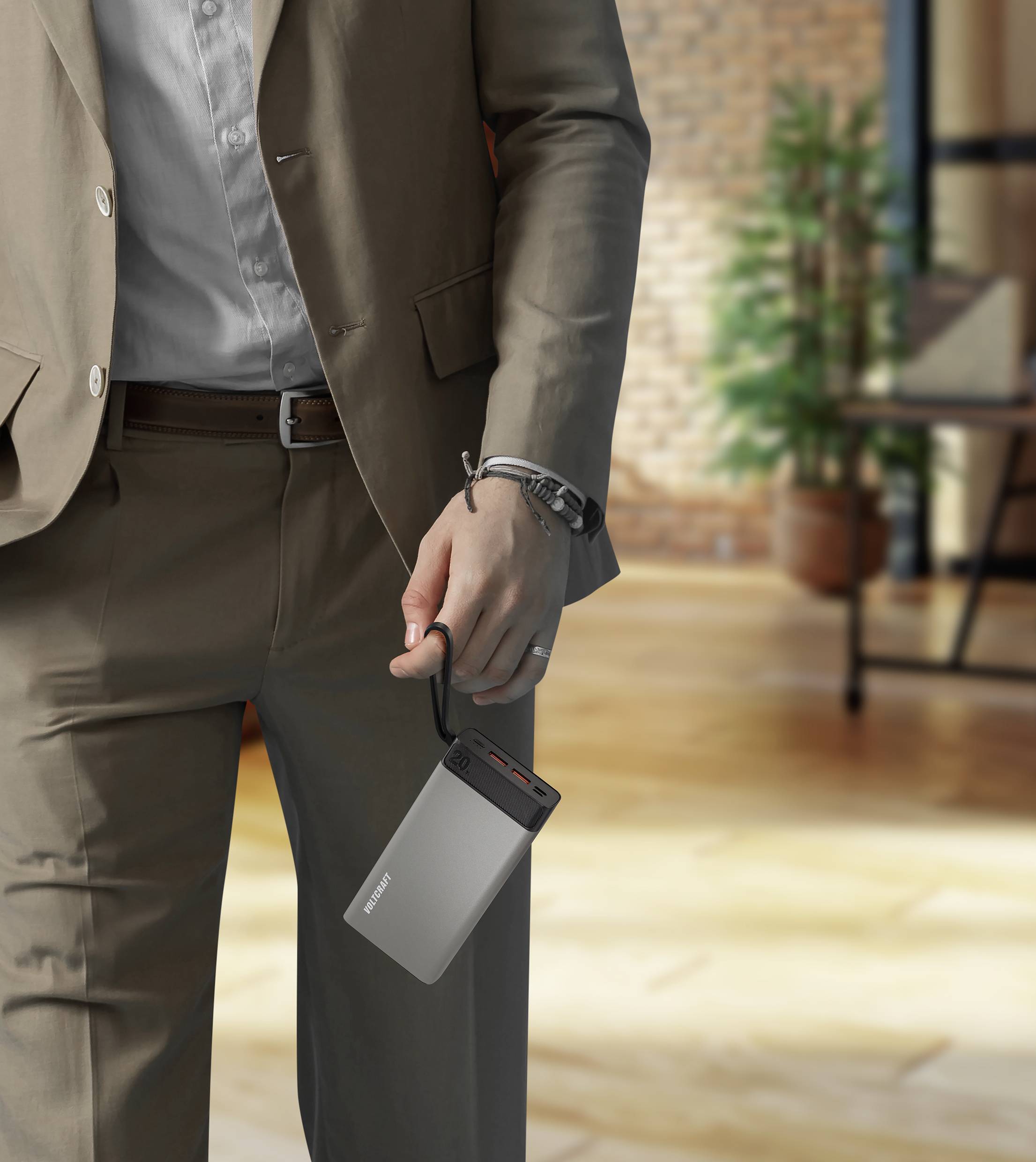 Eine Person in einem Anzug hält eine externe Festplatte in der Hand. Im Hintergrund ist ein Büro mit Holzboden und Topfpflanzen zu sehen.