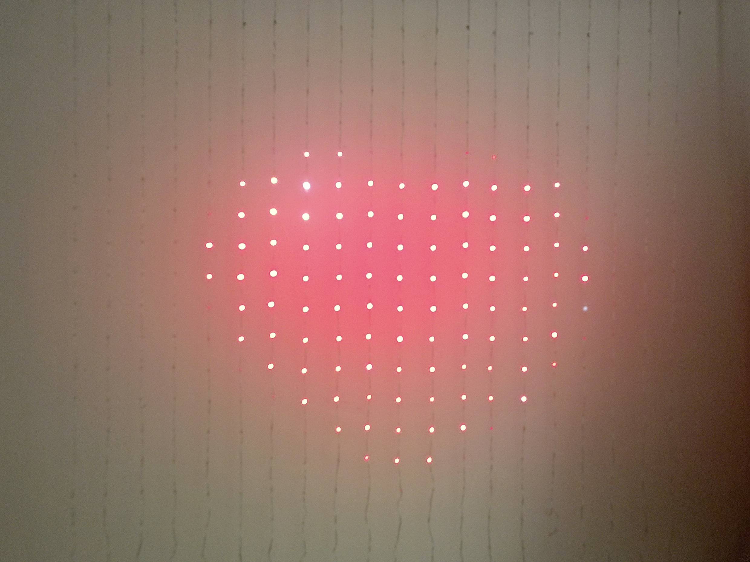 Ein Herzmuster aus roten Lichtern auf einem Raster, beleuchtet auf einer Wand.