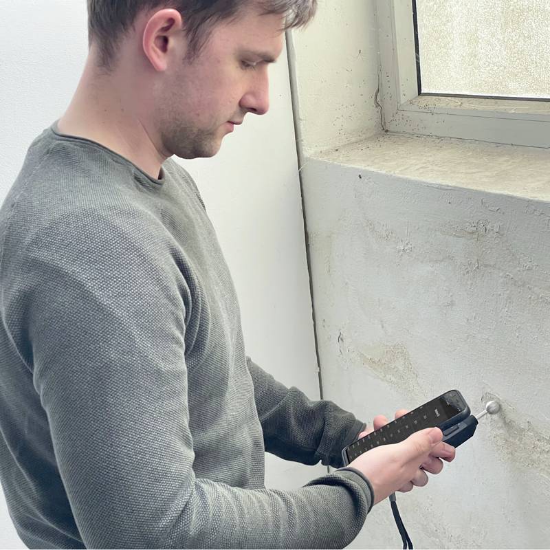 Ein Mann bohrt ein Loch in eine Wand neben einem Fenster und hält einen Bohrer.