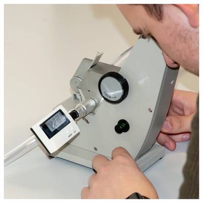 Person passt ein optisches Tischinstrument mit digitaler Anzeige und Fokussierknopf an, während sie/er eine Linsen- oder Röhreneinheit untersucht.