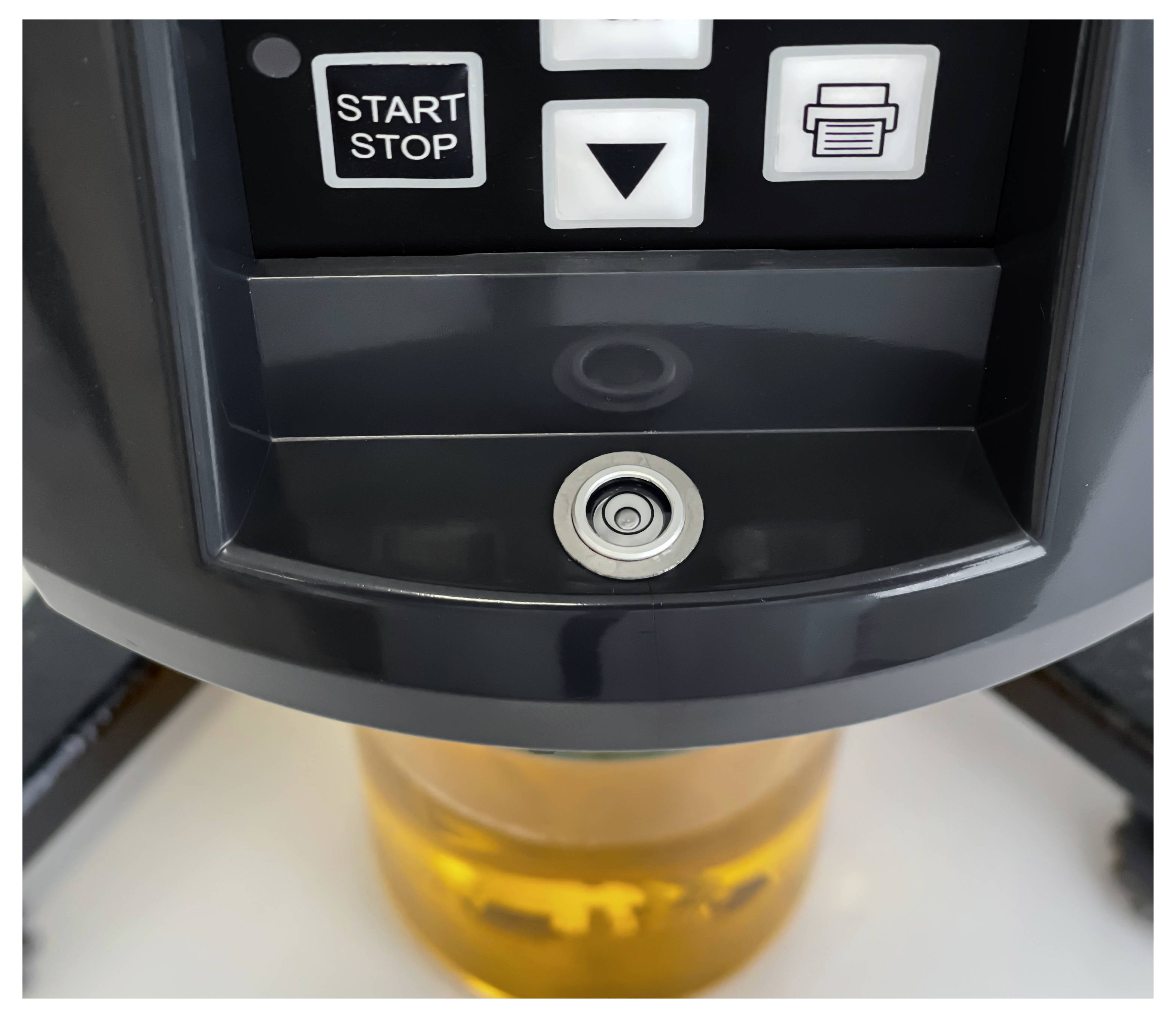 Nahaufnahme eines Kaffeemaschinenbedienfeldes mit "START STOP" und Drucktasten über einer Ausgießer, die ein Glas mit bernsteinfarbener Flüssigkeit füllt.