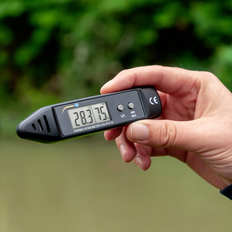 Eine Hand hält ein digitales Thermometer mit einer Anzeige von 28,3 Grad Celsius vor einem unscharfen Hintergrund.