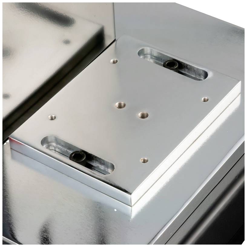 Metallplatte mit Bohrungen, möglicherweise Teil einer Maschineneinrichtung, auf einer reflektierenden Oberfläche montiert.