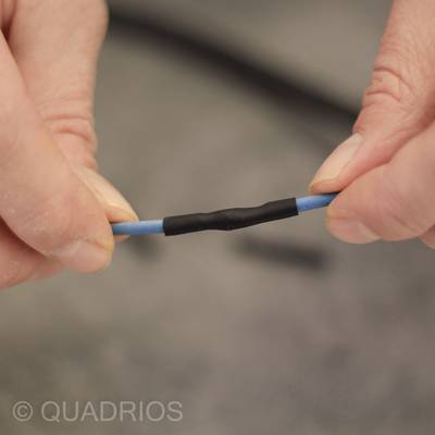 Zwei Hände halten ein blaues Kabel mit einem schwarzen Schrumpfschlauch in der Mitte.