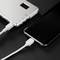 Ein Smartphone wird mit einem weißen Kabel an eine tragbare silberne Powerbank angeschlossen. Beide Geräte liegen auf einer dunklen Oberfläche.