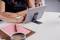Person tippt auf Tablet, das auf einem Ständer auf einem Tisch steht. Daneben liegen ein Notizbuch und eine Tasse Kaffee.