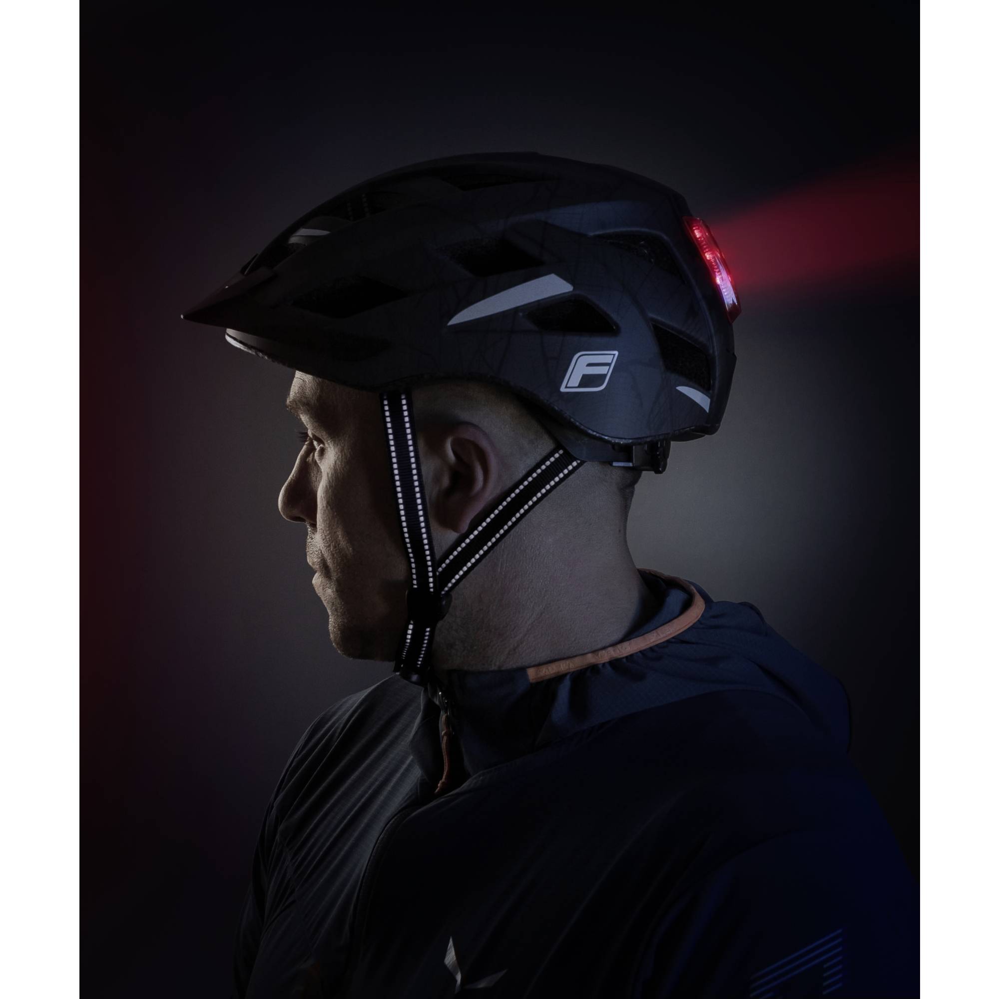 Eine Person trägt einen Fahrradhelm mit rotem Rücklicht. Der Helm ist dunkel und das Licht leuchtet in einem schwach beleuchteten Raum.
