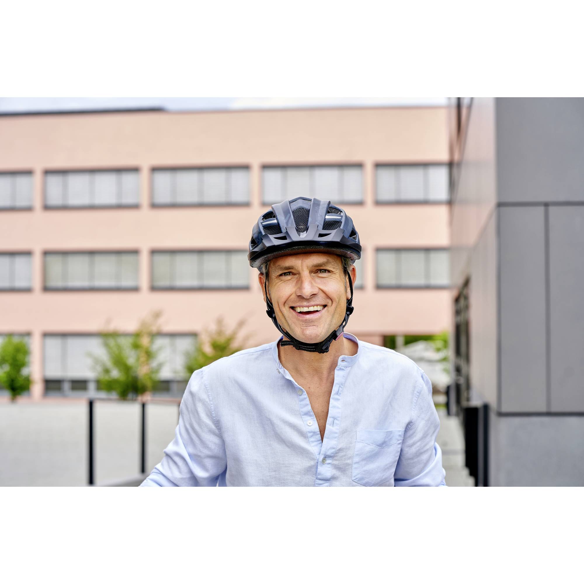 Ein Mann mit Helm lächelt in die Kamera, im Hintergrund ein modernes Gebäude.