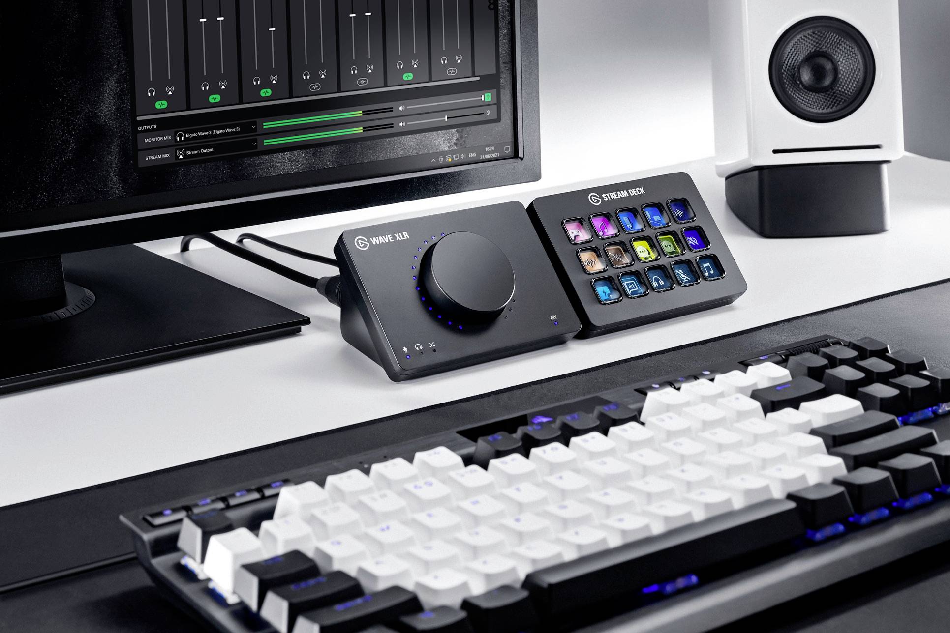 Ein Schreibtisch mit einem Computerbildschirm, Audiomischgerät mit Drehknopf und Tasten, einer Lautsprecherbox und einer Tastatur.