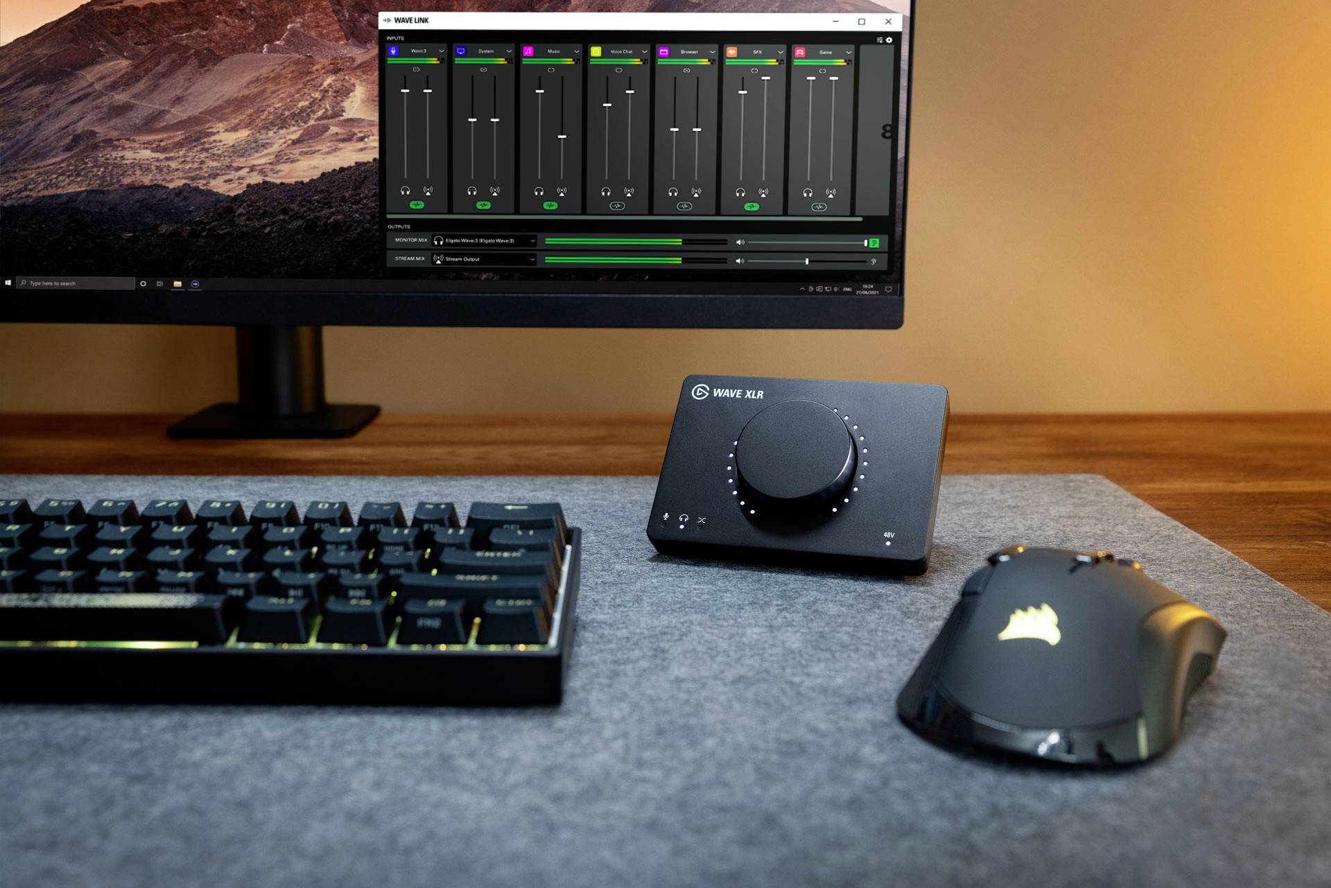 Computertisch mit Monitor, Tastatur, Maus und Audio-Mixgerät. Auf dem Bildschirm wird ein Audiosoftware-Interface angezeigt.