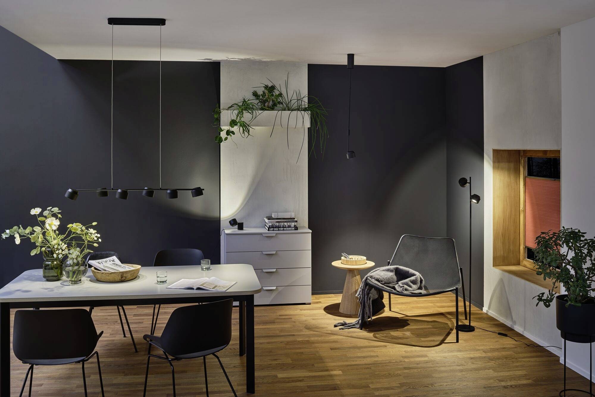 Moderner Essbereich mit Holzboden, dunklen Wänden, einem Esstisch mit vier schwarzen Stühlen. Ein gemütlicher Sessel steht in einer Ecke.