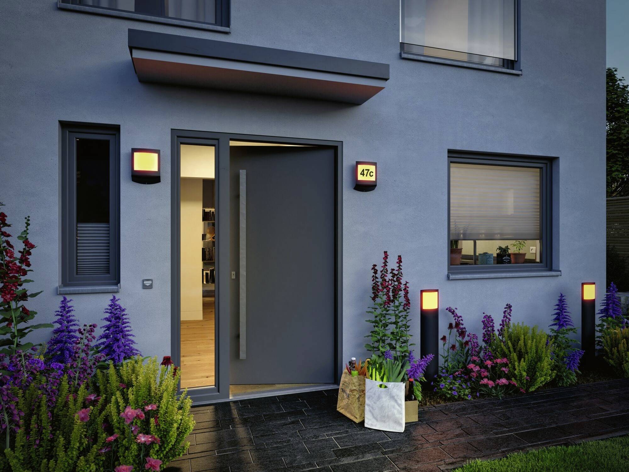 Blumenreiche Eingangstür eines modernen Hauses, leicht geöffnet, mit Hausnummer '47c'. Garten im Vordergrund, beleuchtet am Abend.