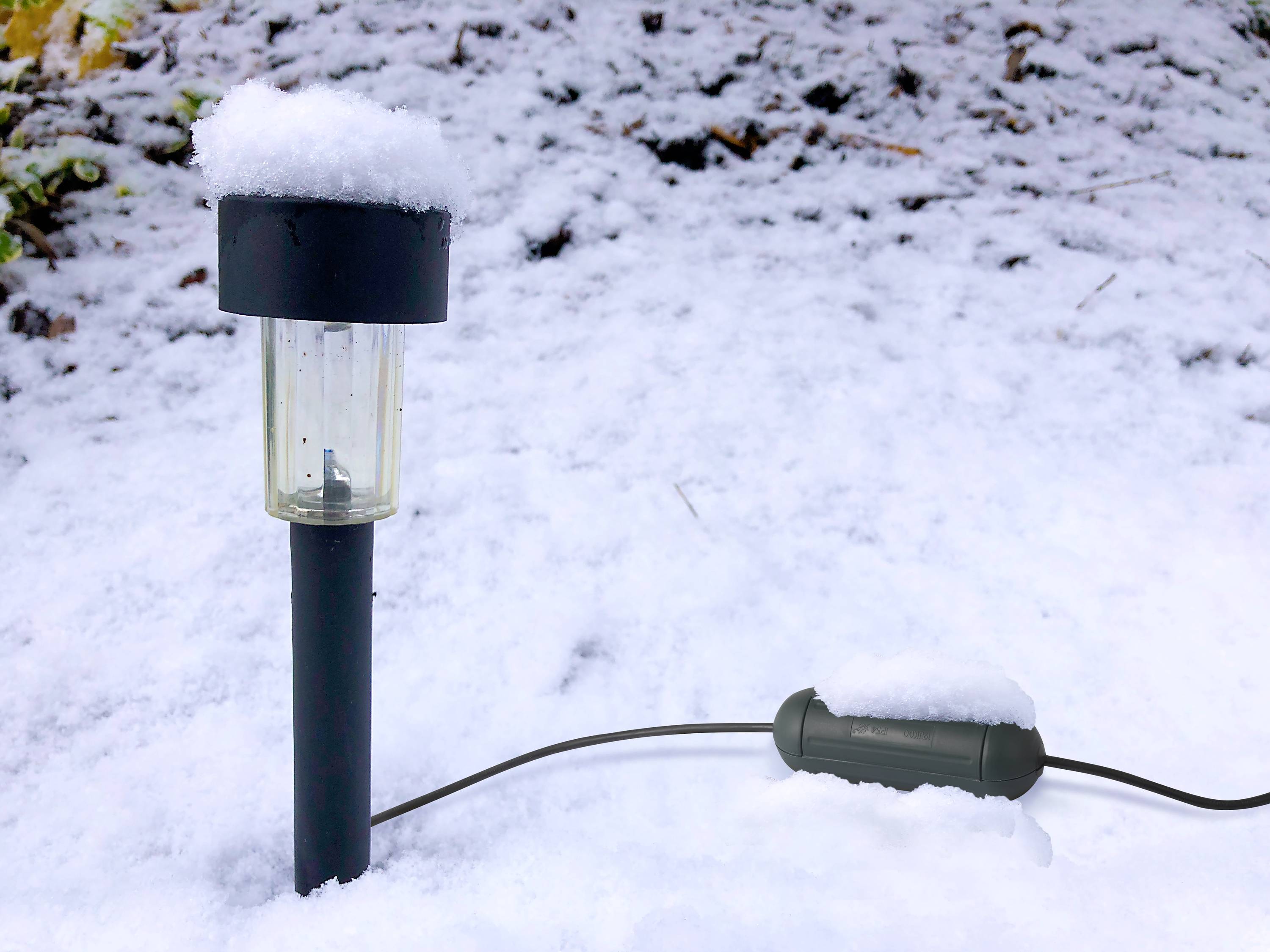 Solarlampe und Kabel im Schnee zeigen Wintervorbereitungen für Außenbeleuchtung.