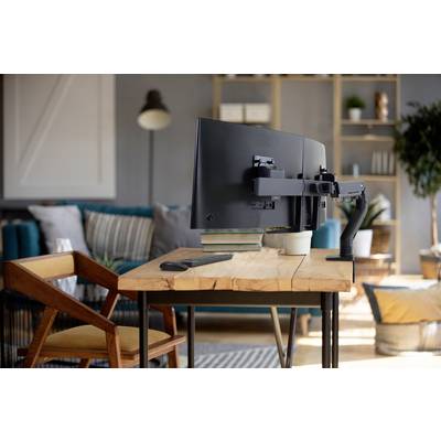 Ein Schreibtisch mit einem großen, an einem Arm montierten Bildschirm steht in einem gemütlichen Wohnzimmer mit Regalen und einem Sessel im Hintergrund.