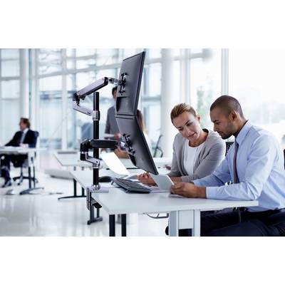 Ein Mann und eine Frau sitzen an einem Schreibtisch in einem modernen Büro und schauen auf ein Tablet. Hinter ihnen sind Arbeitskollegen.