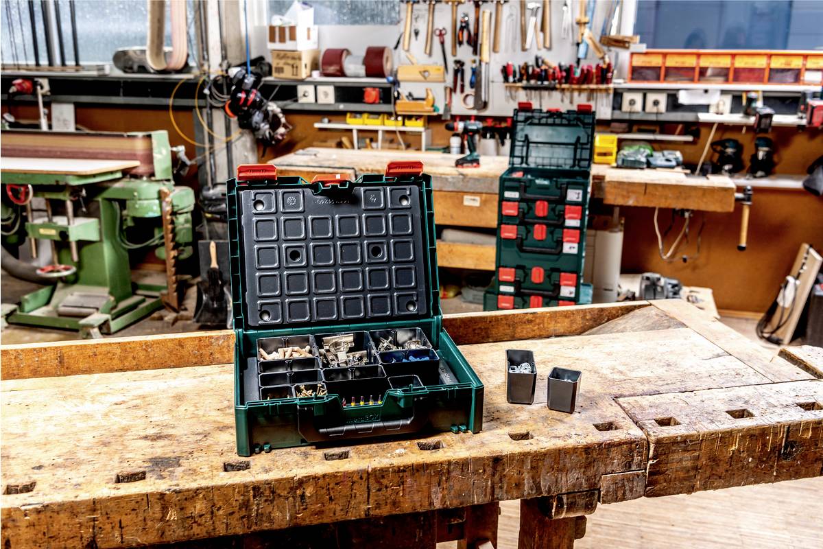 Eine Werkstatt mit Holzbänken, Werkzeug an den Wänden, einer offenen Kiste mit Schrauben und Dübeln auf einem Tisch im Vordergrund.