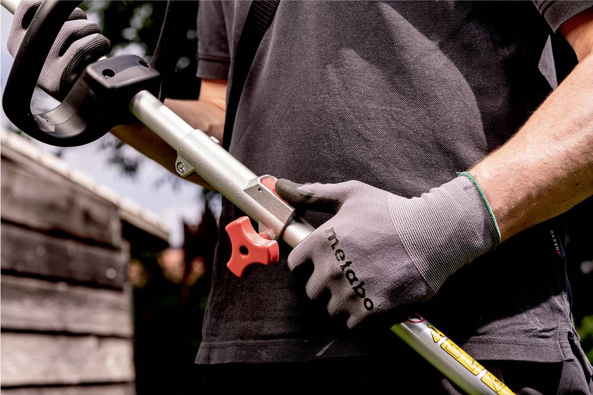 Eine Person trägt Handschuhe und hält ein Gartengerät. Der Fokus liegt auf der Handhabung des Werkzeugs.