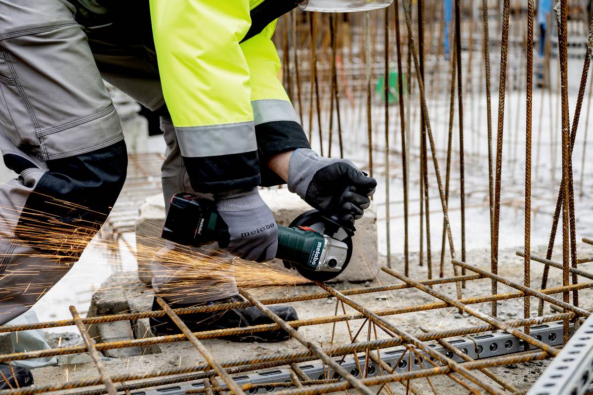 Arbeiter schneidet Metallstäbe mit Winkelschleifer auf Baustelle. Funken sprühen, Arbeiter trägt Sicherheitskleidung.