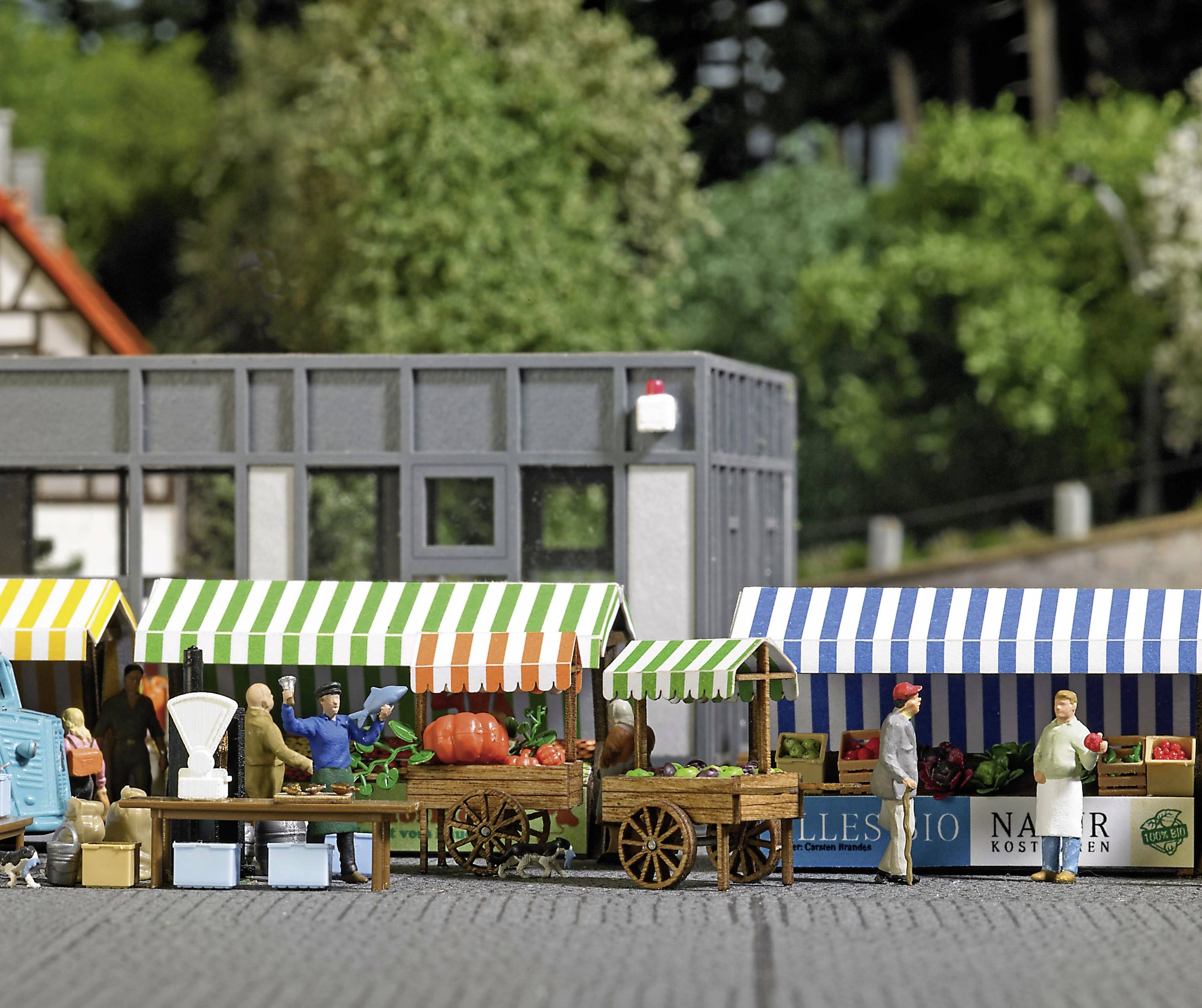 Ein Miniatur-Bauernmarkt mit Gemüse- und Obstständen. Menschen plaudern, einige kaufen ein. Verschiedene Markisen in Grün, Blau und Rot.