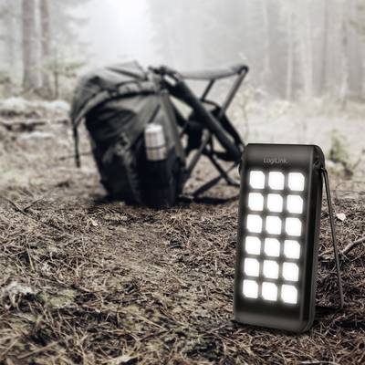 Tragbares LED-Licht im Vordergrund, im Wald aufgestellt; im Hintergrund ein Rucksack und ein Faltstuhl, die auf einen Outdoor-Ausflug hindeuten.