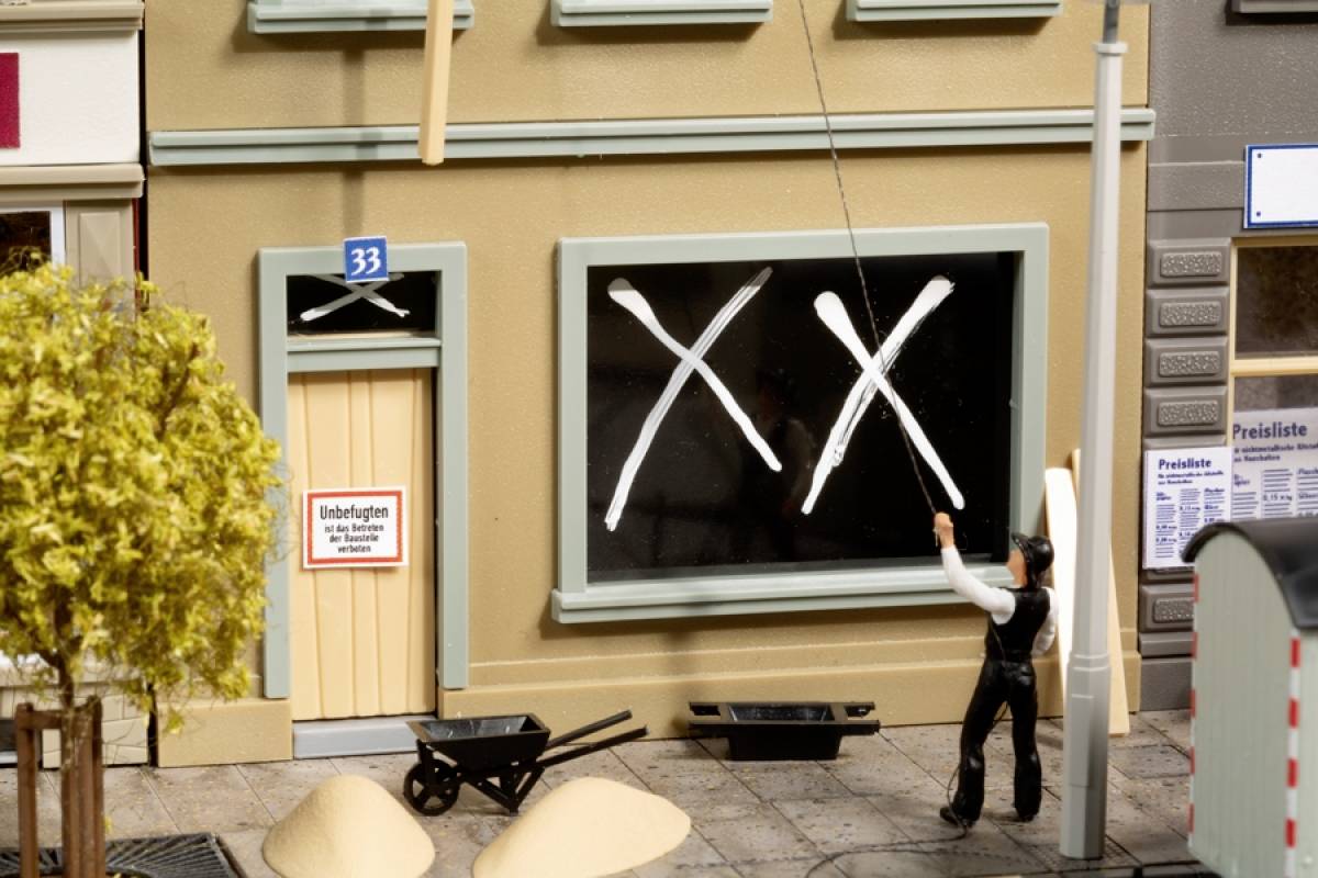 Ein Miniaturmodell zeigt einen Fensterputzer vor einem Gebäude mit schwarzen Kreuzen auf den Scheiben. Ein Schild an der Tür weist auf Umbaumaßnahmen hin.