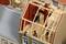 Ein Modellhaus mit teilweise offenem Dach zeigt eine Dachkonstruktion aus Holz. Zwei Figuren arbeiten am Bau des Dachs.